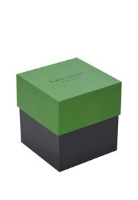 Grön låda med matt yta och präglad "kate spade NEW YORK" logotyp; svart bas, fyrkantig form, ren design, minimalistisch utseende.