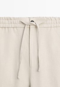 Beige linnen broek met elastische tailleband en gebonden aantrekkoord aan de voorzijde.