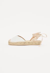 Weißer Espadrille-Schuh mit perforiertem Obermaterial, geflochtener Jutesohle und beigen Knöchelbindungen. Mit abgerundeter Zehenform und flachem Design.