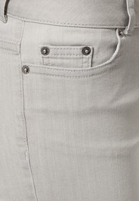 Ljust grå denimtyg med en liten framficka, silverfärgade detaljer och en slät yta med ett subtilt twillmönster.