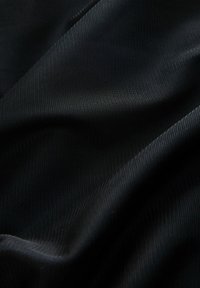 Schwarzer strukturierter Stoff mit gewebtem Muster, der glatte und leicht glänzende Oberflächen aufweist und eine subtile Tiefe und Dimension erzeugt.