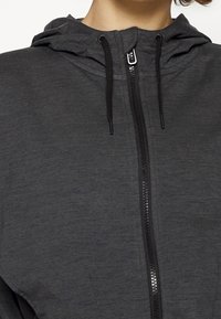 Mörkgrå zip-up hoodie med huva, med svarta dragsnören och en slät yta. Närbild av dragkedjedetaljen.