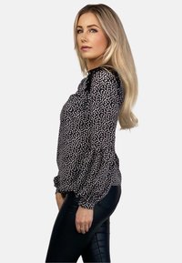 Czarna bluzka w biały plamisty wzór, z bufkami i okrągłym dekoltem, w zestawieniu z dopasowanymi czarnymi legginsami. Gładka tekstura.
