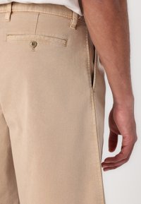 Los pantalones de algodón beige cuentan con un bolsillo trasero con cierre de botón, bolsillos laterales y una textura suave con un corte ajustado.