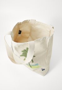 Beige kanvas totebag med palmetreedesign, hvite bomullsmapper og en romslig innvendig plass. Har en merkelapp i innerlommen.
