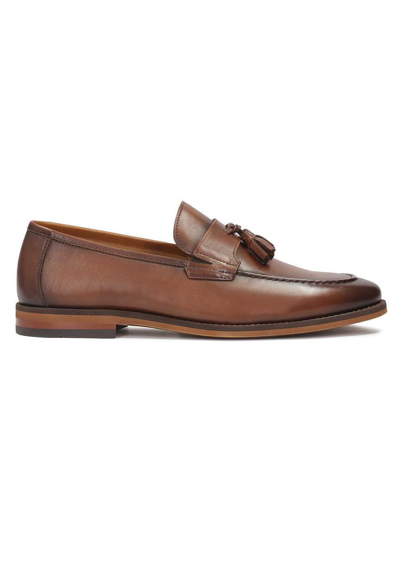 Mocasines de cuero marrón con detalle de borlas, punta redondeada y suela de un marrón claro en contraste. Textura suave y diseño minimalista.