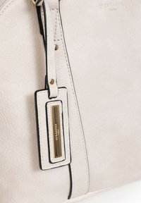 Borsa a mano in pelle beige con una finitura testurizzata, caratterizzata da un bordo scuro, hardware in oro e un'etichetta rettangolare con branding in rilievo.
