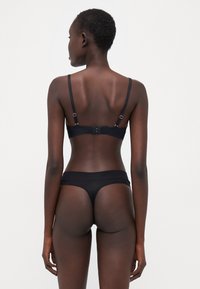 Black bra and thong set with adjustable straps, seamless design, and soft texture. Minimalist style with no visible hardware details.