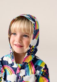 Colorful raincoat featuring a navy base, rainbow and cloud patterns, a pink zipper, and a hood. Smooth, waterproof material with vibrant design.