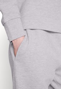 Gray ribbed fabric sweatshirt and joggers with a relaxed fit, featuring a side pocket and subtle texture in the material.