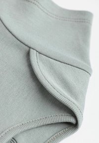 Tessuto grigio chiaro con una texture liscia e un orlo arrotolato. Presenta cuciture ordinate e un design aderente e sagomato.