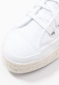 Sneaker bianco in tela con superficie texture, lacci piani e occhielli rotondi in metallo. Presenta una suola in juta naturale intrecciata per una maggiore presa.