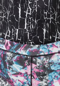 Gros plan de deux motifs de tissu : noir avec une texture craquelée blanche en haut, formes géométriques multicolores en rose, bleu et gris en bas.