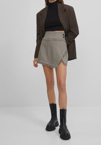 Spódnica w kratę z postrzępionym dołem, wysoki stan i detalem z guzikami, zestawiona z czarnym golfem i masywnymi czarnymi botkami.