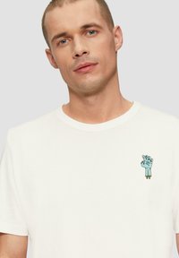 Witte katoenen t-shirt met een kleine blauwe handgrafiek geborduurd op de linkerkant van de borst, met een klassieke ronde halslijn en korte mouwen.