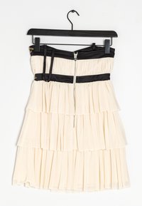 Krämfärgad strapless klänning med svarta satin accenter, lager av veckad design och silverdetalj i dragkedjan. Hänger på en svart krok.