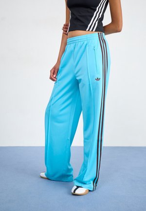 Person wearing light blue wide-leg track pants with brown stripes, black cropped tank top, and white slip-on shoes.
