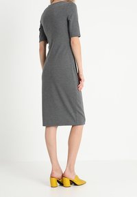 Robe en tricot gris à manches courtes et coupe mi-longue. Associée à des mules jaunes à talons blocs. Texture lisse, silhouette ajustée.