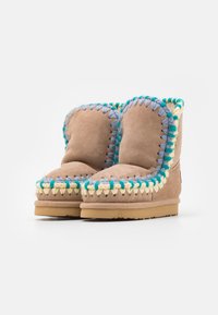 Botas de tobillo de ante marrón con costuras decorativas en azul, verde y amarillo, de forma redondeada y textura suave. Suelas de goma planas.
