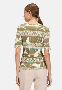 Brown short-sleeve top featuring a geometric pattern with white, green, and blue accents. Smooth fabric with a fitted design.