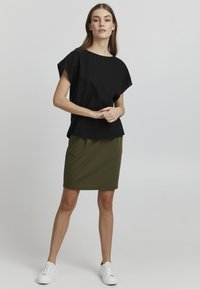 Maglietta nera a taglio rilassato con maniche corte, abbinata a una gonna verde oliva aderente e sneaker bianche con lacci. Design semplice e pulito.