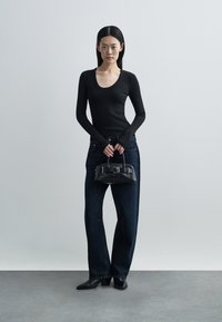 Top preto de mangas compridas com riscas, jeans escuros de ganga de cintura alta, mala de mão preta em pele com alça pequena e botins pretos de salto.