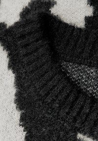 Tessuto lavorato a maglia bianco e nero con una consistenza morbida e pelosa; presenta un motivo audace e accenti a coste. Vista ravvicinata del design.