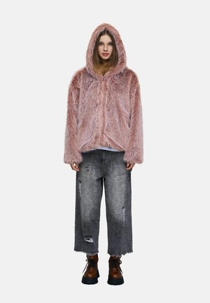 Jeune femme portant une veste à capuche rose et duveteuse, un jean large gris à motifs avec des déchirures, et des chaussures marron à lacets, debout face à l'avant.