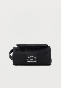 Black fabric bag with a zip closure and a front label patch. Features a rectangular shape and a side handle for easy carrying.