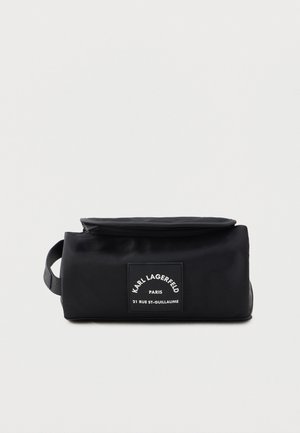 Czarna torba materiałowa z zamknięciem na zamek i przednią łatką z etykietą. Posiada prostokątny kształt oraz boczną rączkę ułatwiającą przenoszenie.