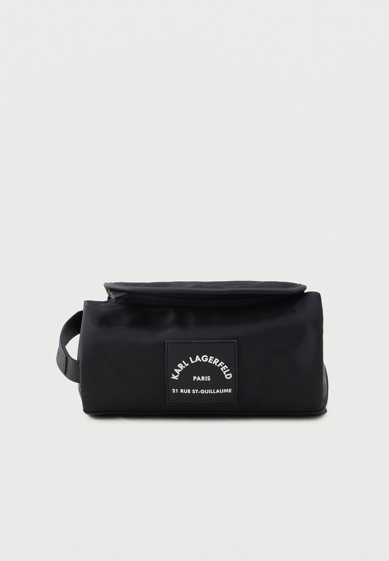 Black fabric bag with a zip closure and a front label patch. Features a rectangular shape and a side handle for easy carrying.