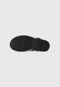 Semelle de chaussure noire avec un motif de grip texturé, dotée de crêtes et de rainures de flex pour une traction, conçue pour la durabilité et la stabilité.