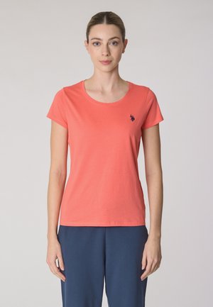T-shirt corallo a maniche corte in cotone morbido con scollatura rotonda e piccolo logo blu navy sul lato sinistro del petto. Abbinato a pantaloni blu scuro.