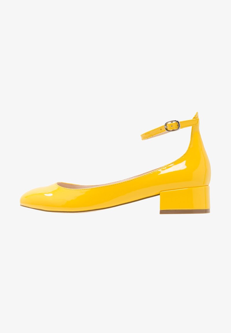 Chaussure à talon bas en cuir verni jaune avec bride à la cheville et boucle argentée, bout rond et talon bloc sur fond blanc.
