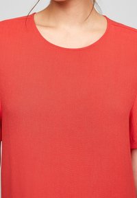 Top rojo de manga corta con cuello redondo, hecho de una tela suave y texturizada. Presenta un corte holgado y un diseño sencillo.