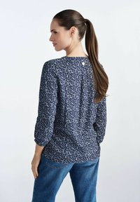 Granatowa bluzka w kwiatowy wzór, okrągły dekolt, guziki z tyłu oraz rękawy o długości 3/4. Połączona z dżinsami.