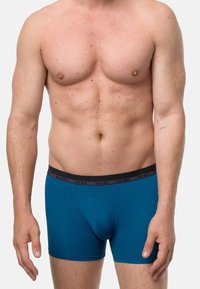 Modré boxerky s černým elastickým pasem s nápisem „nurder“. Látka vypadá hladká a přiléhavá. Žádné vzory nejsou viditelné.