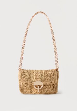 Petit sac à main en paille tissée avec un fermoir circulaire doré et une bandoulière chaîne, présenté sur un fond uni.