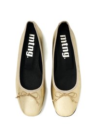 Ballerines dorées avec une texture lisse, bout arrondi et un fin nœud à l'avant. Semelles intérieures noires avec un marquage blanc à l'intérieur.