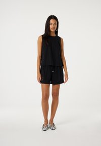 Zwarte mouwloze top met een A-lijn ontwerp, gecombineerd met zwarte short met trekkoord. Schoeisel heeft een patroon in een gestructureerd ontwerp.