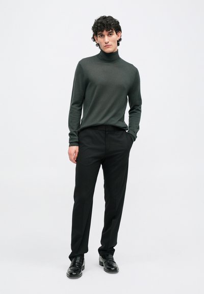 Tamsiai žalios spalvos golfas derinamas su juodais pritaikytais kelnėmis. Avalynė - juodi odiniai slip-on'ai. Paprastas, elegantiškas dizainas su lygu tekstūra.