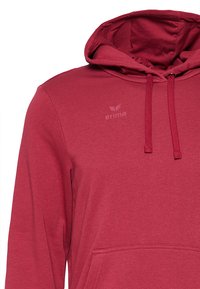 Felpa bordeaux con cappuccio regolabile, tasca frontale e logo 'erima' discreto. Realizzata in tessuto morbido e textured. Vestibilità regolare.