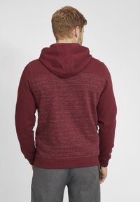 Felpa con cappuccio bordeaux e retro strutturato con strisce orizzontali. Realizzata in tessuto morbido, con polsini e orlo a coste, presenta un design casual.