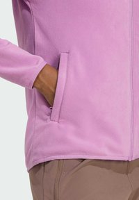 Helle rosa Fleecejacke mit Reißverschluss, Seitentaschen und glatter Textur. Verfügt über lange Ärmel und einen geschwungenen Saum.