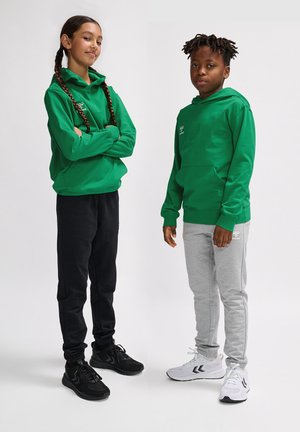 Groene hoodie-sweaters met voorzakken, gecombineerd met zwart en grijs trainingsbroeken. Met zwarte en witte sportschoenen en vlechten.