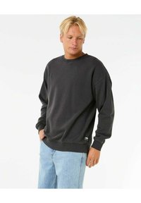 Sudadera negra de manga larga y cuello redondo, fabricada con un material suave. Presenta puños y dobladillo acanalados, y un pequeño detalle de logo.