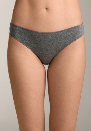 Femeie purtând lenjerie de bumbac gri simplă, de tip bikini, văzută de la talie până la partea superioară a coapselor, pe un fundal neutru.