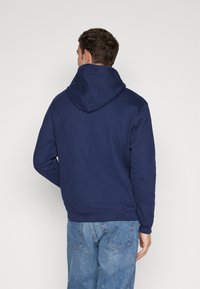 Hanorac cu glugă de culoare bleu marin, dintr-un material moale, având un buzunar kangaroo și mansete ribbate, asortat cu blugi de culoare bleu deschis.
