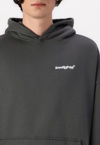 Sweat à capuche gris en matière douce, doté d'une poche kangourou et d'un petit logo blanc sur la poitrine. Design simple avec capuche à cordon de serrage.