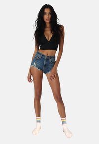 Top corto nero, pantaloncini di jeans strappati e calze crema con strisce arcobaleno. Focalizzati sulle trame e sui contrasti di colore.